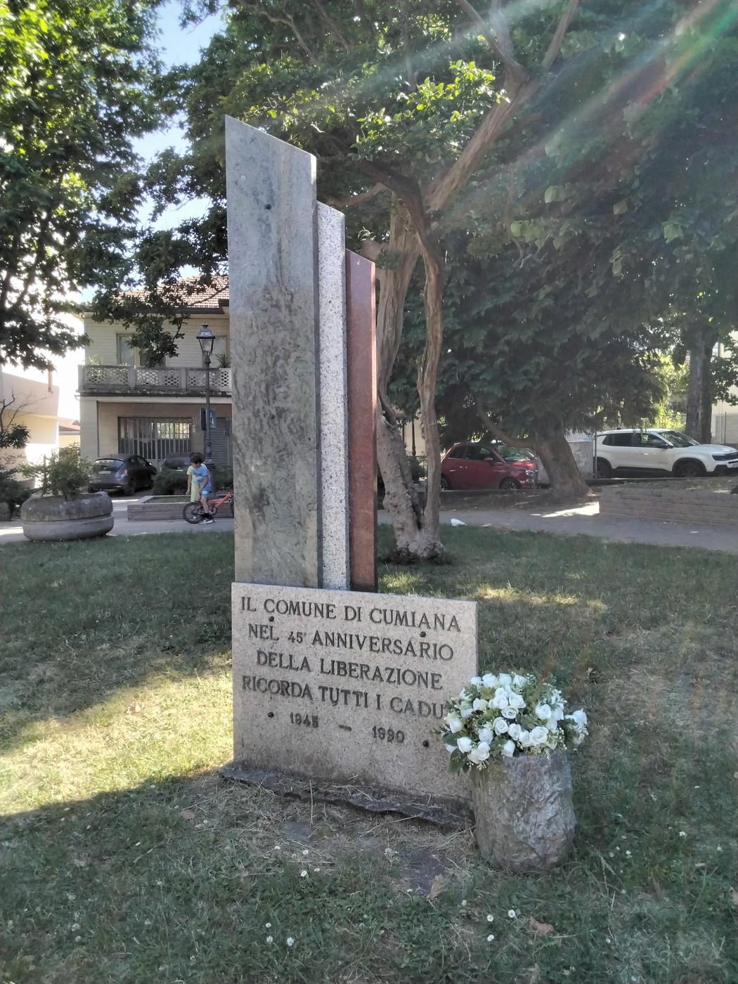 Cippo commemorativo per il 45° anniversario della Liberazione, con fiori e alberi circostanti.