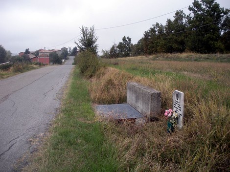 Lapide commemorativa in un'area rurale, circondata da erba e un viale tranquillo.