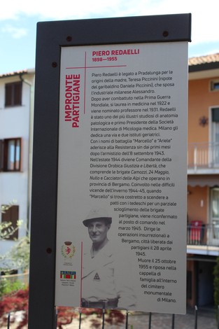 Impronta partigiana dedicata a Piero Redaelli, con pannello informativo e sfondo di un edificio.