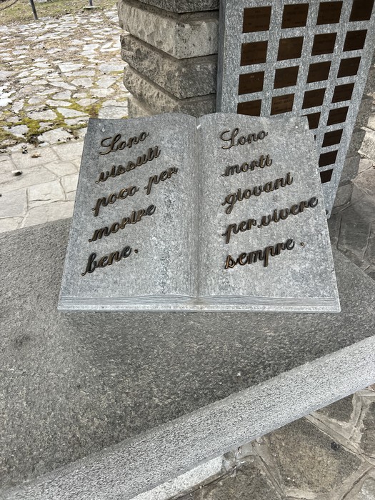 Libro in pietra a pagine aperte con iscrizione, posato su un basamento in granito.