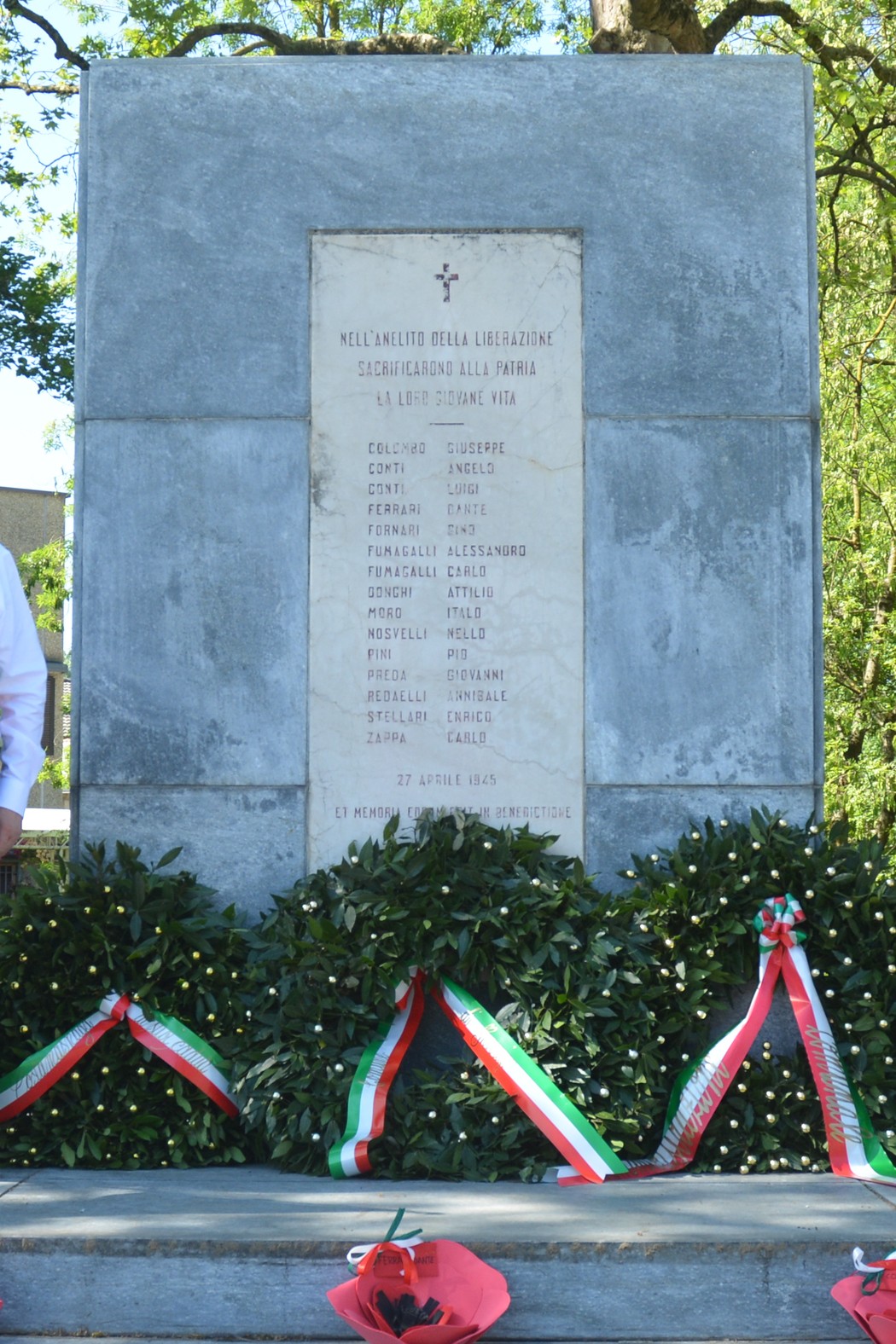 Monumento ai partigiani con un elenco di nomi, circondato da decorazioni floreali e nastri tricolore.