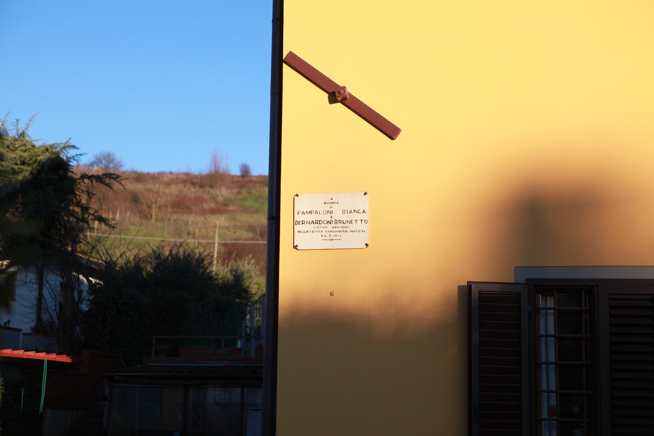 Lapide commemorativa dedicata a Pampaloni e Bernardoni su una parete gialla, in un contesto rurale.