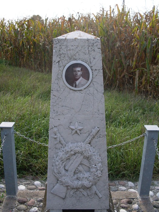 Cippo commemorativo a Mori, con immagine e simboli dedicati a un caduto. Circondato da un campo di grano.