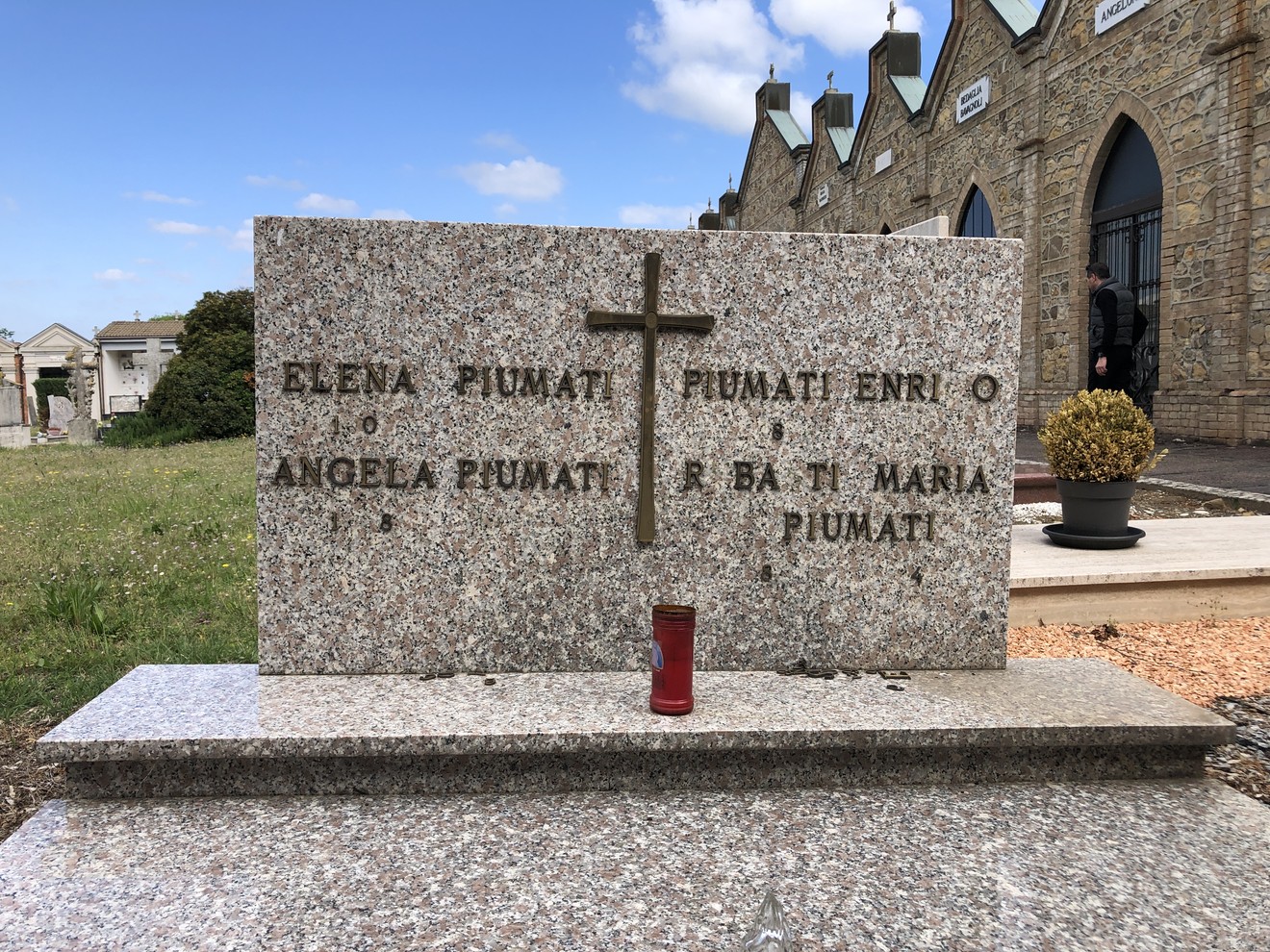 Sepolcro di Piumini, con croce e candele, situato in un cimitero storico.