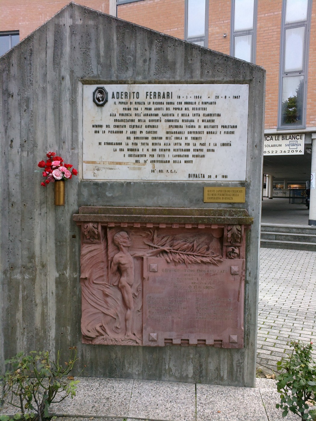 Lapide commemorativa dedicata a Aderito Ferrari, inserita in un contesto urbano.