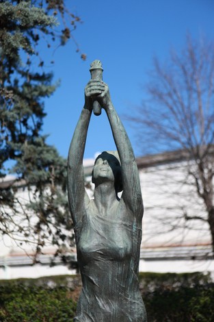 Monumento alla 63° Brigata Garibaldi, statua in bronzo con figura femminile che solleva un ramo. Sullo sfondo, cielo azzurro.