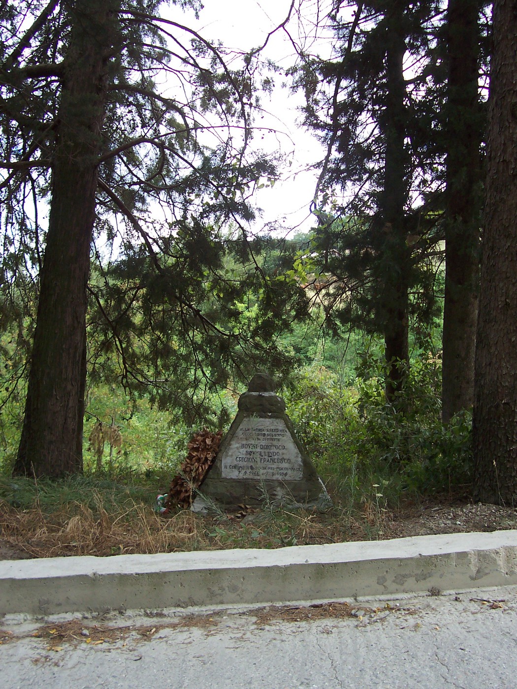 Cippo commemorativo immerso nel verde, circondato da alberi, in un contesto naturale suggestivo.