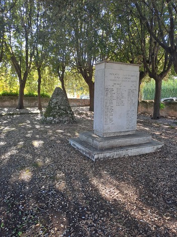 Monumento ai caduti di Pontasserchio, circondato da alberi eombra, con iscrizioni commemorative su un basamento.