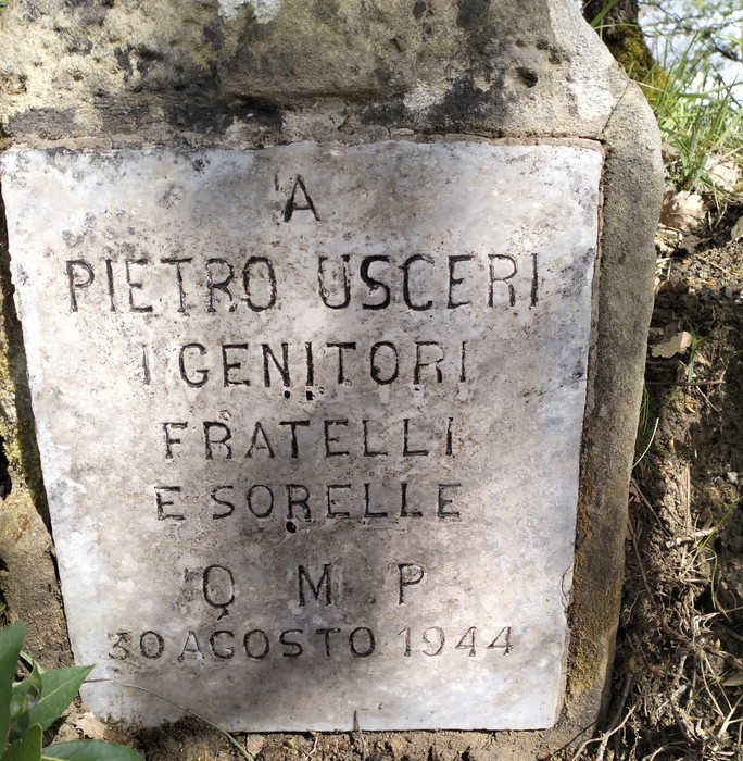 Cippo commemorativo dedicato a Pietro Uscieri, situato in un contesto naturale.