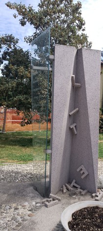Monumento alla Resistenza con elementi in pietra e vetro, situato in un parco verdeggiante.