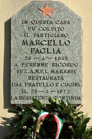Lapide commemorativa di Marcello Paglia, partigiano, con una stella e decorazioni in tricolore.
