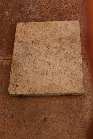 Lapide commemorativa in pietra su muro, con scritte illeggibili e usura evidente. Atmosfera storica e contemplativa.