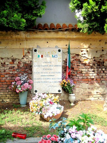 Lapide commemorativa in onore dei fucilati, adornata con fiori e bandiera italiana.