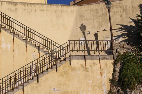 Scorcio di una scala con parapetti, murales e una lampione sullo sfondo, in un contesto urbano.