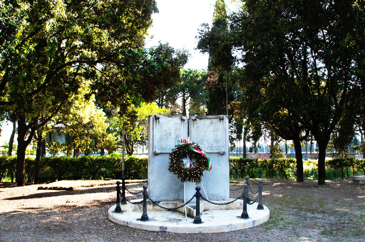 Monumento ai caduti circondato da alberi, con una corona d'alloro su una base di marmo.