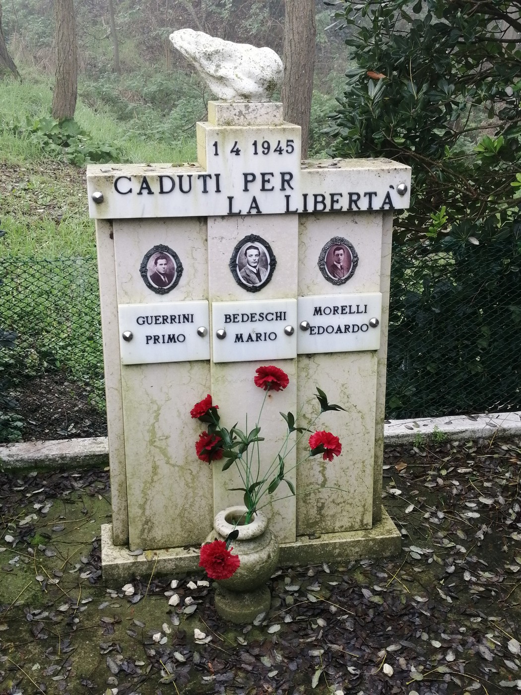 Monumento in memoria di Guerrini, Bedeschi e Morelli, caduti per la libertà nel 1945, con fiori rossi.
