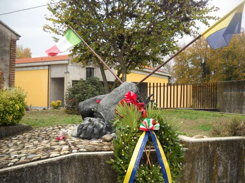 Monumento ai caduti per la Resistenza, decorato con fiori e bandiere tricolori in un ambiente vivace.