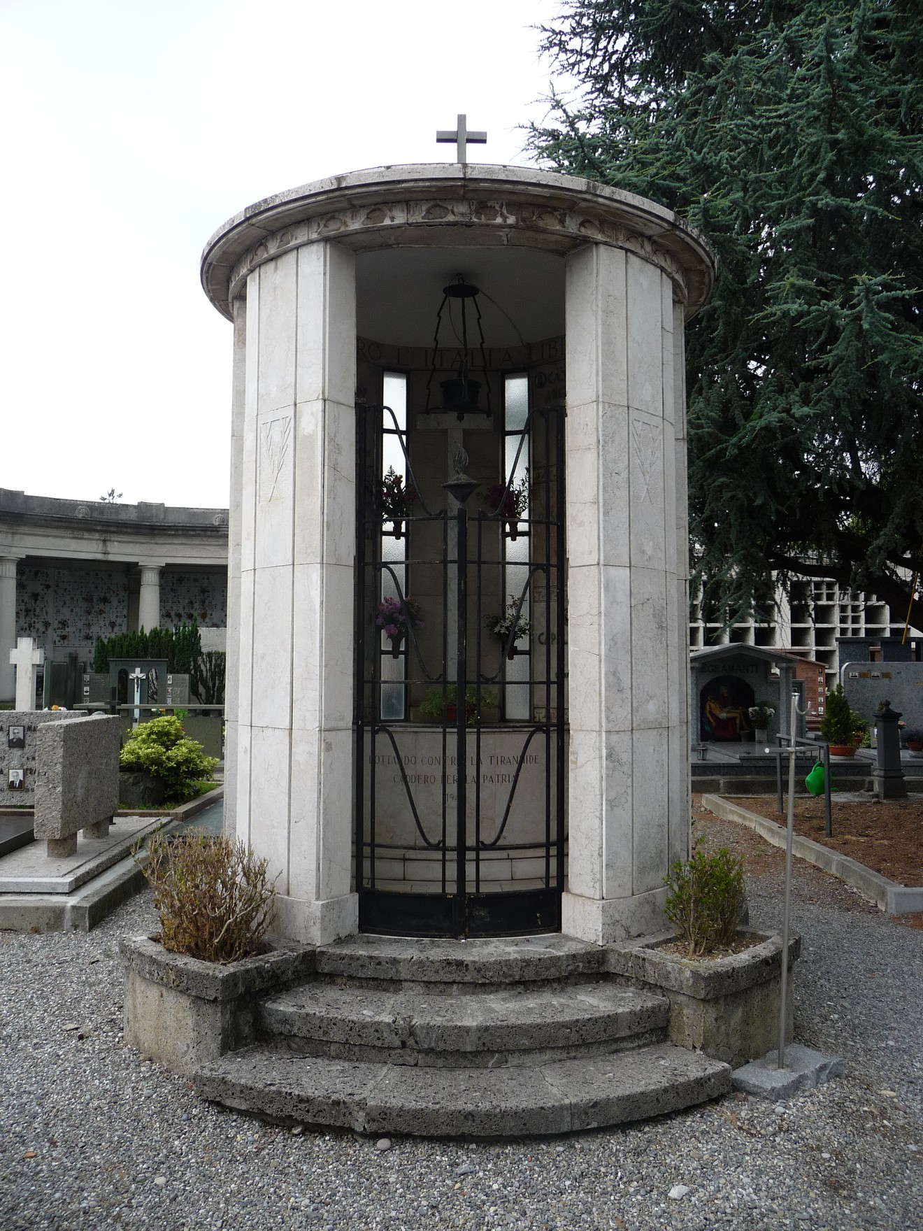 Monumento in stile architettonico elegante, dedicato ai caduti partigiani, circondato da lapidi e vegetazione.