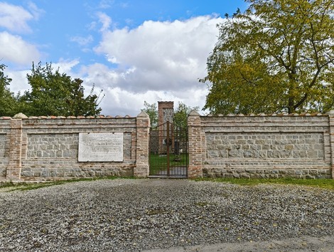 Ingresso al Cimitero di Casaglia, caratterizzato da una recinzione in pietra e un paesaggio verdeggiante.