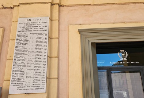 Lapide commemorativa con nomi dei caduti, situata su una parete esterna, in memoria di un conflitto.