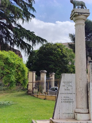 Monumento ai granatieri con iscrizioni commemorative, immerso in un verdeggiante paesaggio romano.