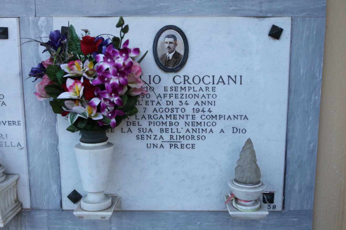 Sepolcro di Mario Crociani, decorato con fiori e una targa commemorativa in marmo.