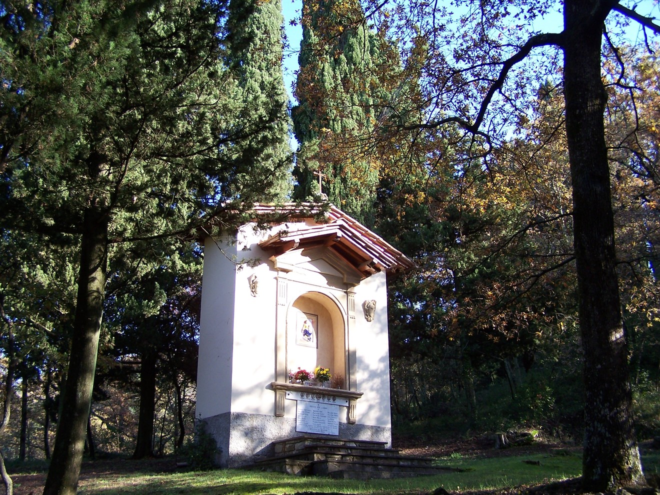 Tabernacolo di Montefiano immerso nella natura, circondato da alberi e luce filtrata.