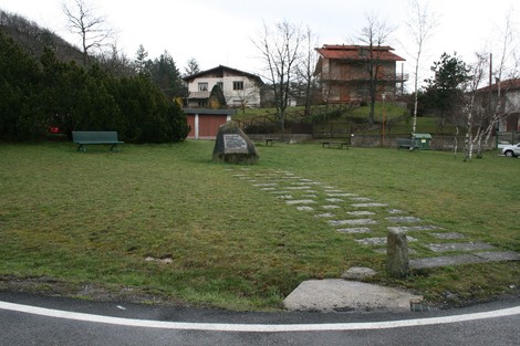 Monumento dedicato ai partigiani e alla popolazione, immerso in un'area verde con panchine e case sullo sfondo.