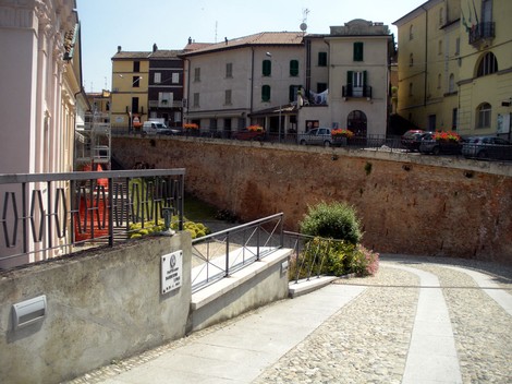 Vista della lapide a Barberini, situata in un contesto urbano con edifici e fiori. Atmosfera storica e suggestiva.