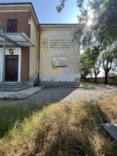 Lapide commemorativa ai partigiani a San Giuliano Vecchio, affiancata da un edificio storico in un contesto verde.