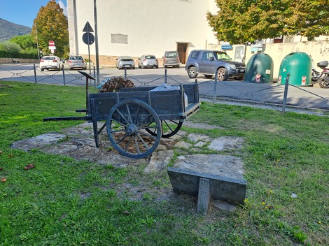 Carretto in legno delle lavandaie, posizionato su una base di pietra, circondato da verde e automobili.