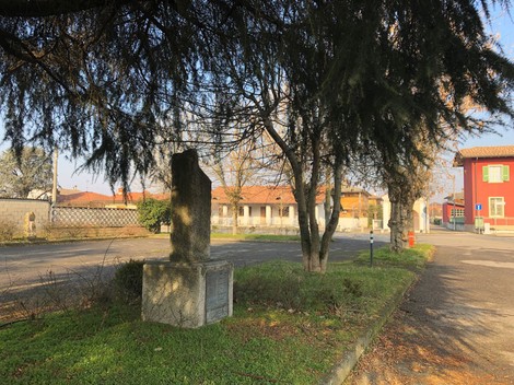 Monumento ai caduti immerso in un tranquillo paesaggio urbano, circondato da alberi e edifici.