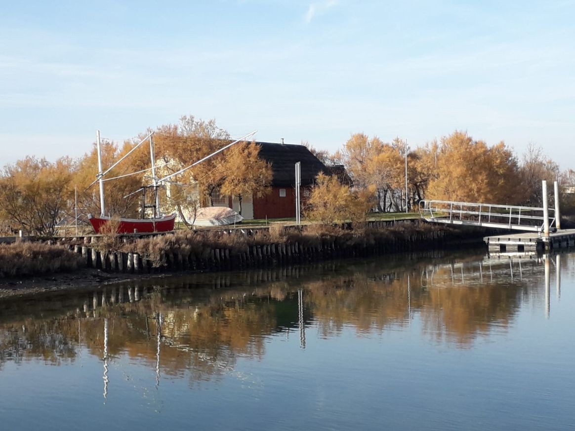 Isola degli Spinaroni: paesaggio con riflessi sull'acqua, barca rossa e alberi autunnali.
