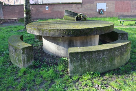 Monumento alla Resistenza con struttura circolare circondata da sedute in pietra immerso nel verde.
