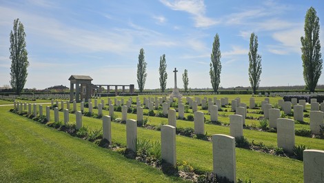 Cimitero di guerra di Argenta, con tombe in fila, alberi alti e cielo blu sereno. Tranquillità e memoria.