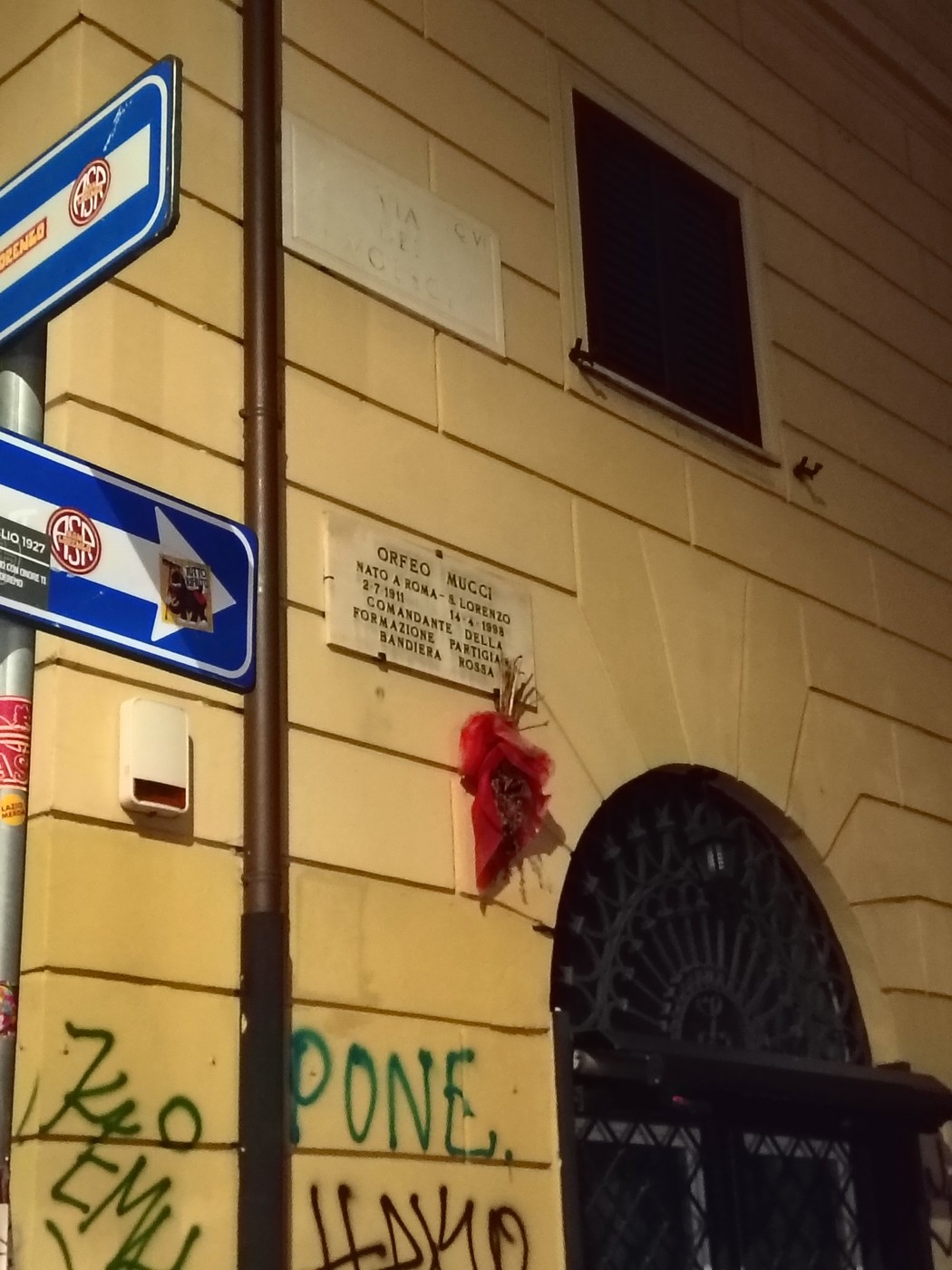 Lapide commemorativa di Orfeo Mucci su un muro vicino a segnali stradali e graffitimille a Roma.