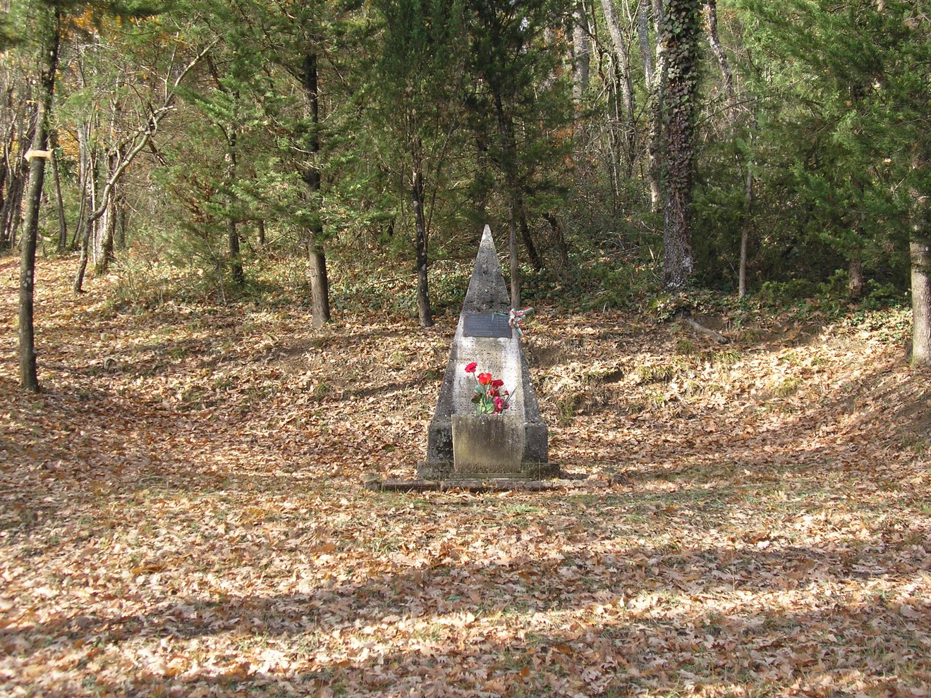 Cippo commemorativo del podere La Casella, immerso nella natura e circondato da foglie secche.