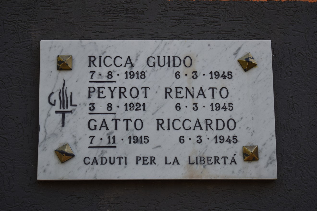 Lapide commemorativa in marmo con nomi di tre individui caduti per la libertà, decorata con simboli metallici.
