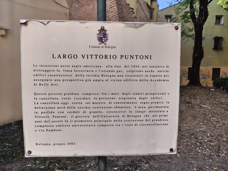 Targa commemorativa in metallo con stemma e iscrizione, fissata su parete esterna in un cortile.
