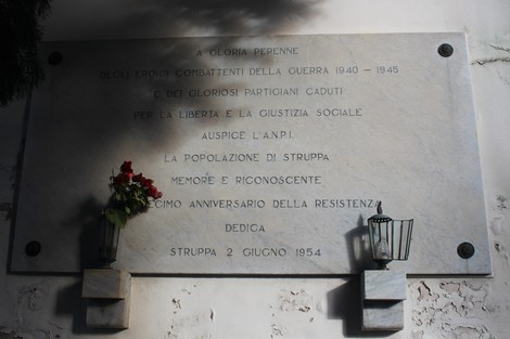 Lapide commemorativa ai caduti per la libertà di Struppa, con fiori e luci decorative.