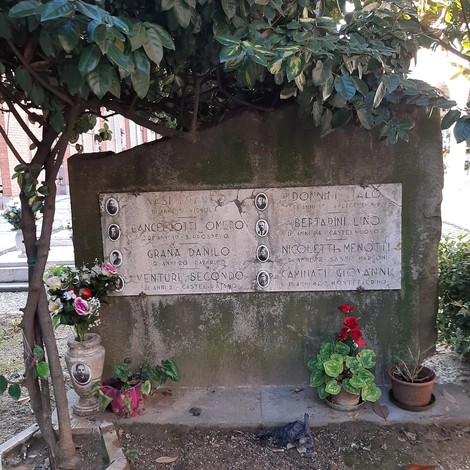Monumento in pietra commemorativo dedicato alle vittime dell'eccidio di Pratomaggiore, con nomi incisi e decorazioni floreali.