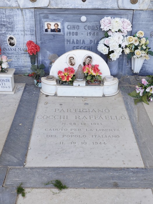 Tomba di marmo con lapide incisa, foto dei defunti, fiori e ritratto di un partigiano.