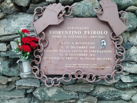 Targa commemorativa dedicata a Fiorentino Peirolo, partigiano, con fiori e decorazioni su una parete di pietra.