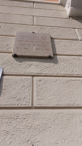 Lapide commemorativa a Gelmi, incastonata in una parete muraria, con informazioni storiche e date significative.