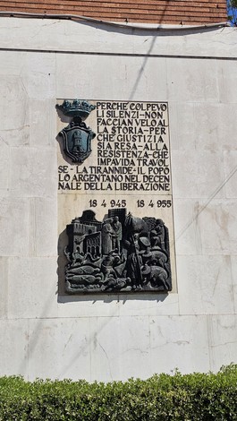 Lapide commemorativa del decennale, con rilievi che celebrano la resistenza e la liberazione.