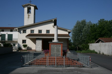Cippo commemorativo di Anchione, con la chiesa sullo sfondo e un recinto di protezione attorno al monumento.