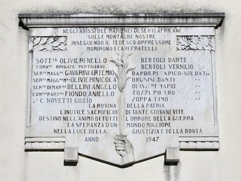 Lapide commemorativa ai caduti di Mocrone, con iscrizioni e decorazioni, situata in un contesto montano.