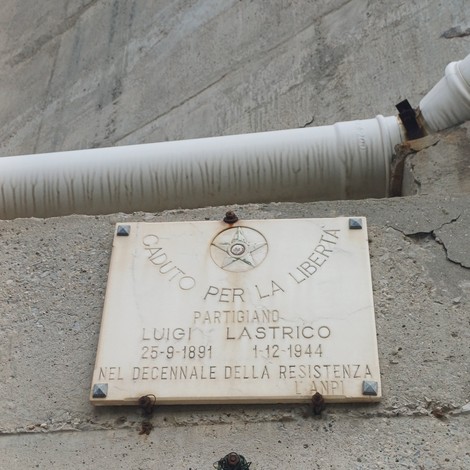 Lapide marmorea con stella e iscrizione, fissata a parete di cemento sotto un grosso tubo bianco.