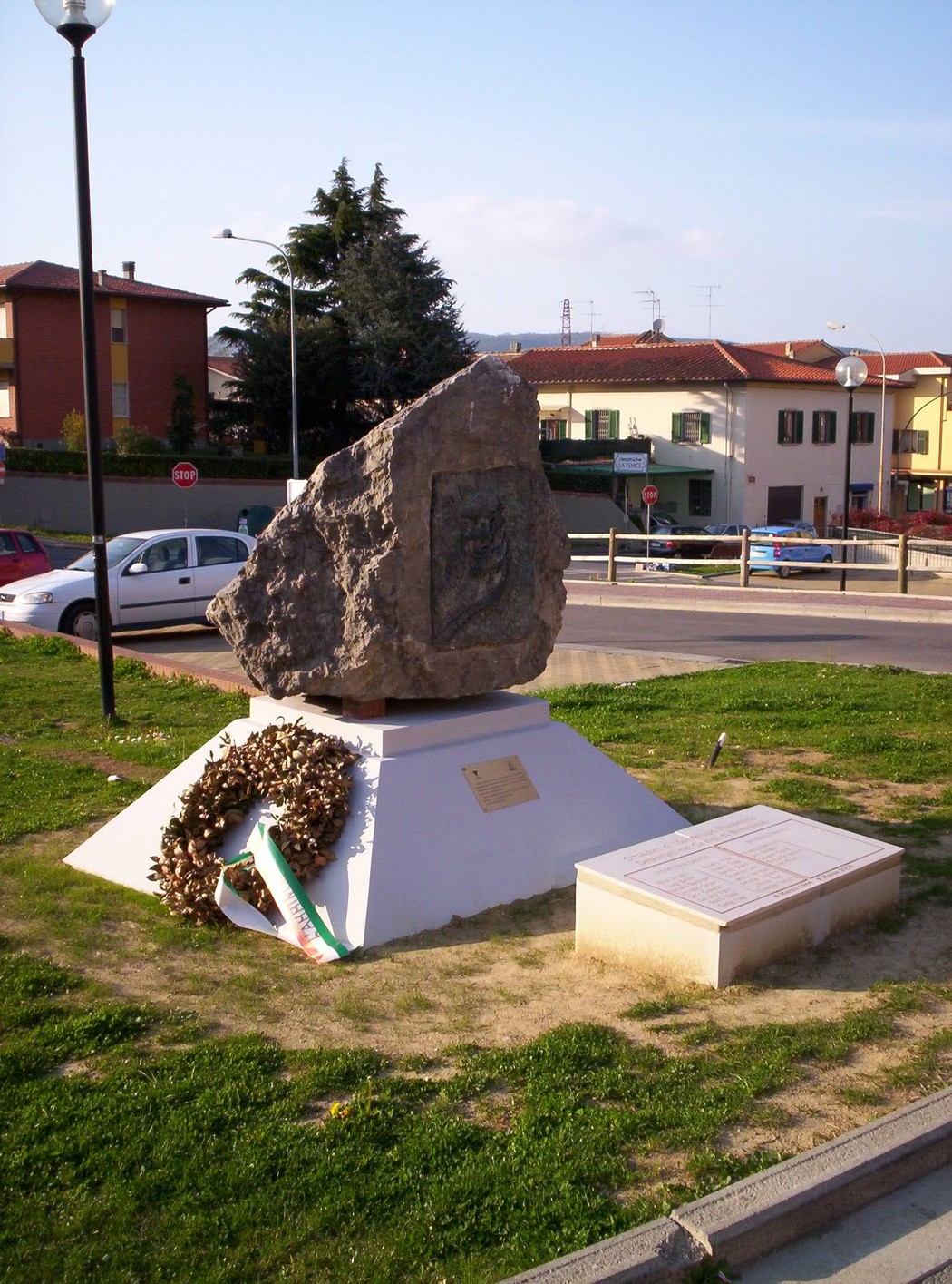 Monumento "Macigno di Gusen" dedicato alla memoria, situato in un'area verde con una corona di fiori.