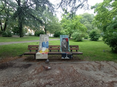 Due panche con opere d'arte, circondate da vegetazione e uccelli, in un tranquillo parco.